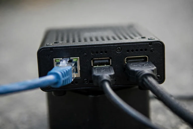 Close-up of the back of a mini PC showing Ethernet, USB and HDMI ports with cables connected